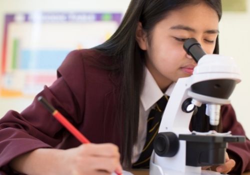 Female Student Using Microscope In Science Class